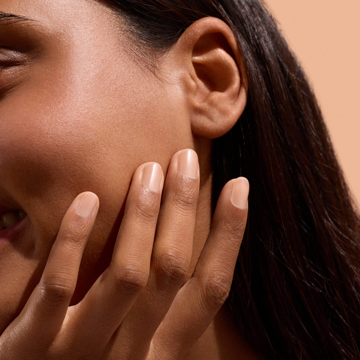 Main aux ongles nude touchant la joue